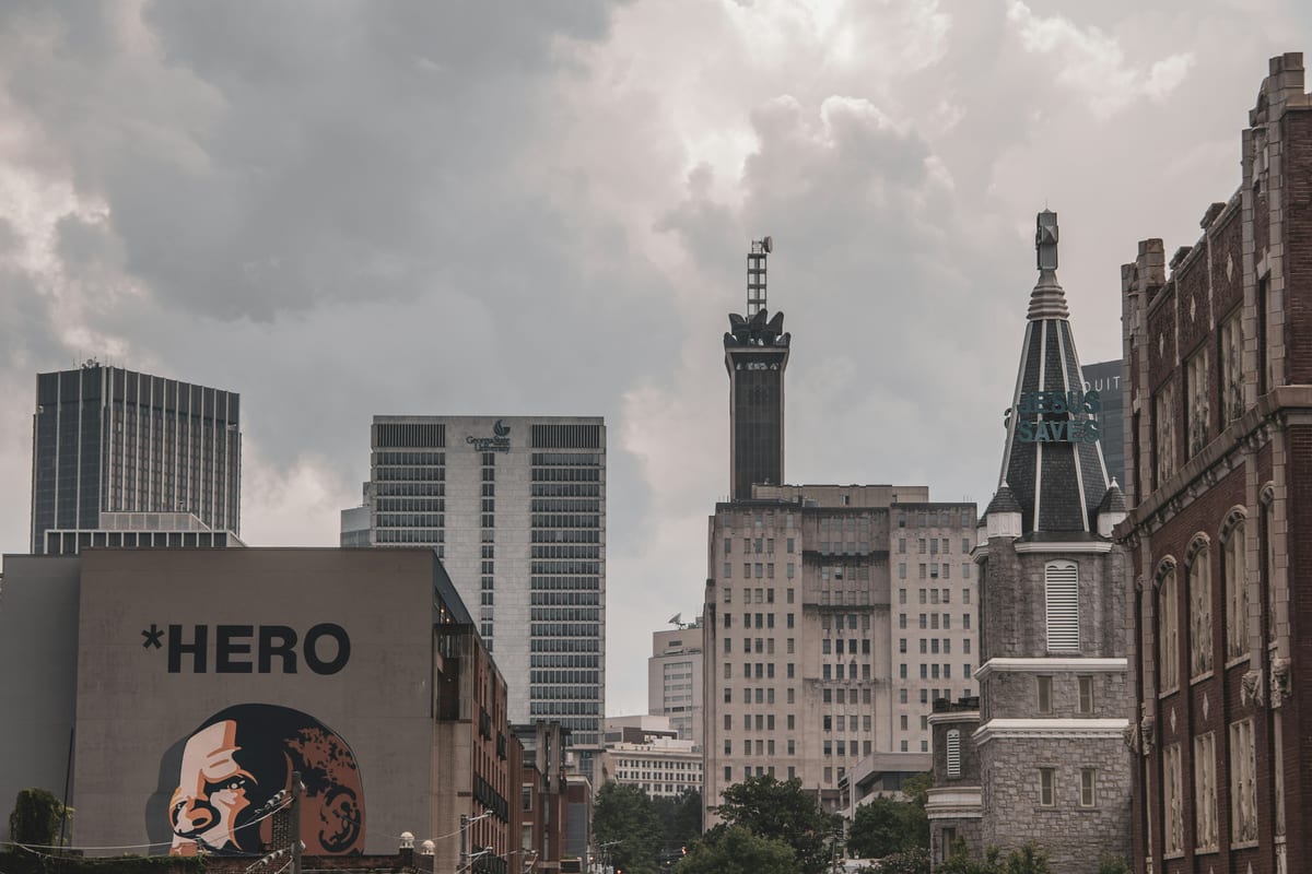 Downtown towers and older stone buildings under a gray sky, with a painted mural in front