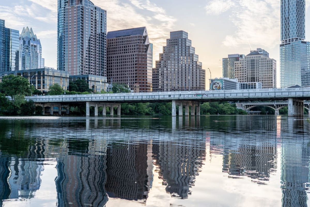A skyline and a low bridge reflected in a still river