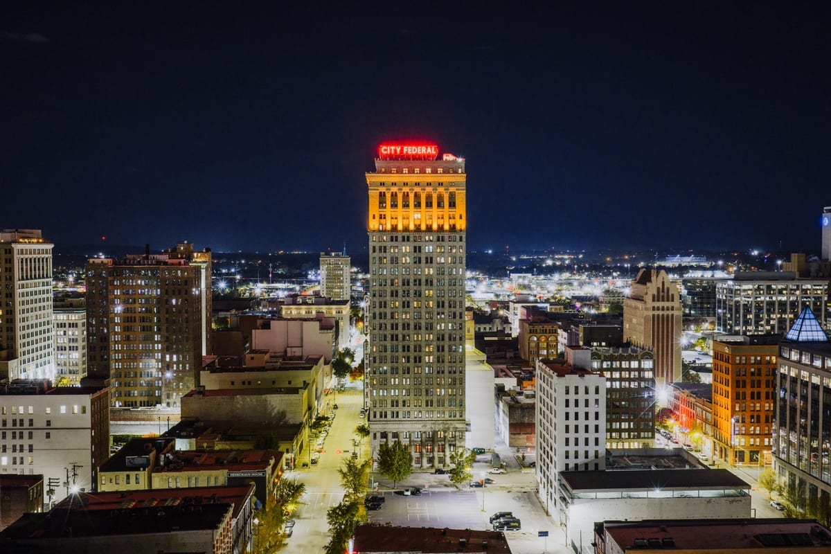 A night view down a lit street toward a tower with a neon sign on its roof