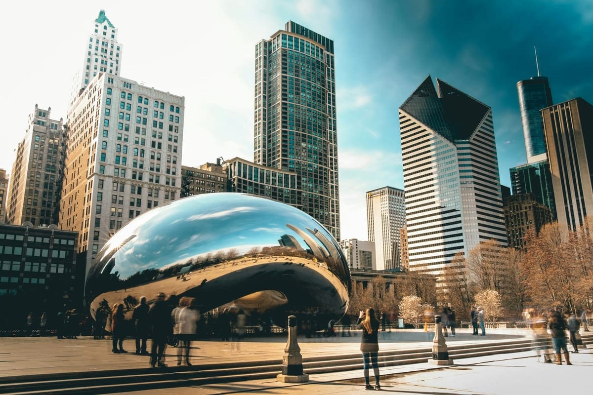 A large mirror-polished sculpture in a plaza, reflecting the skyscrapers around it