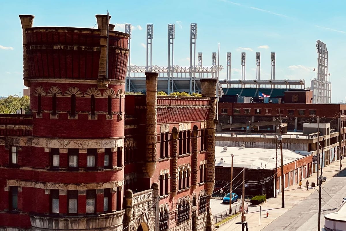 A red-brick building with a round turret, with the light towers of a ballpark beyond