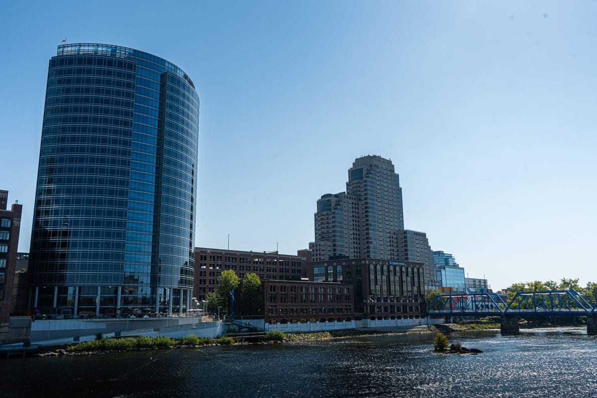 A curved glass tower and a stepped glass building beside a river