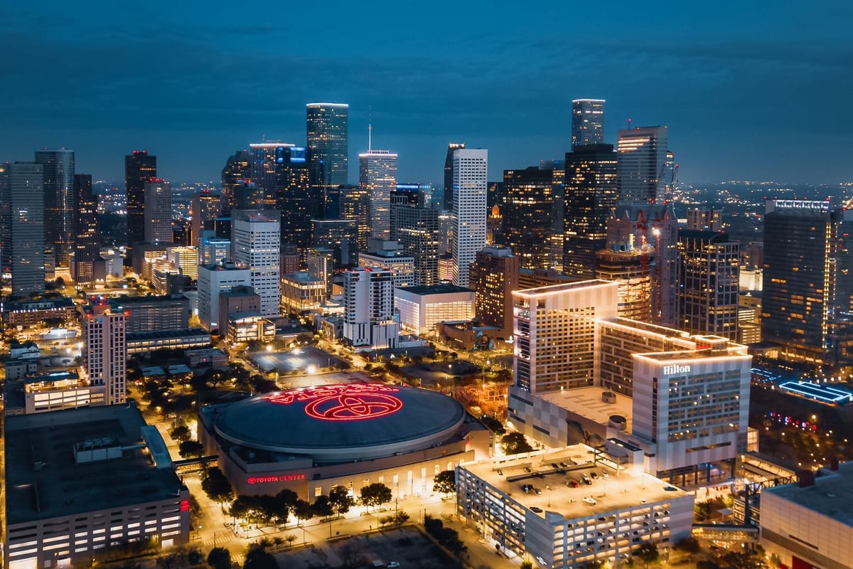 Downtown towers lit at night, seen from above, with a round arena roof in front