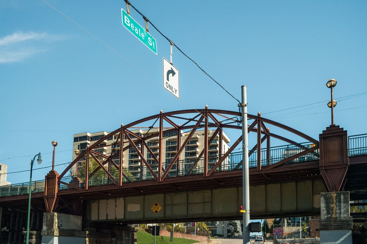 A steel truss bridge, with a street sign on a pole in the foreground