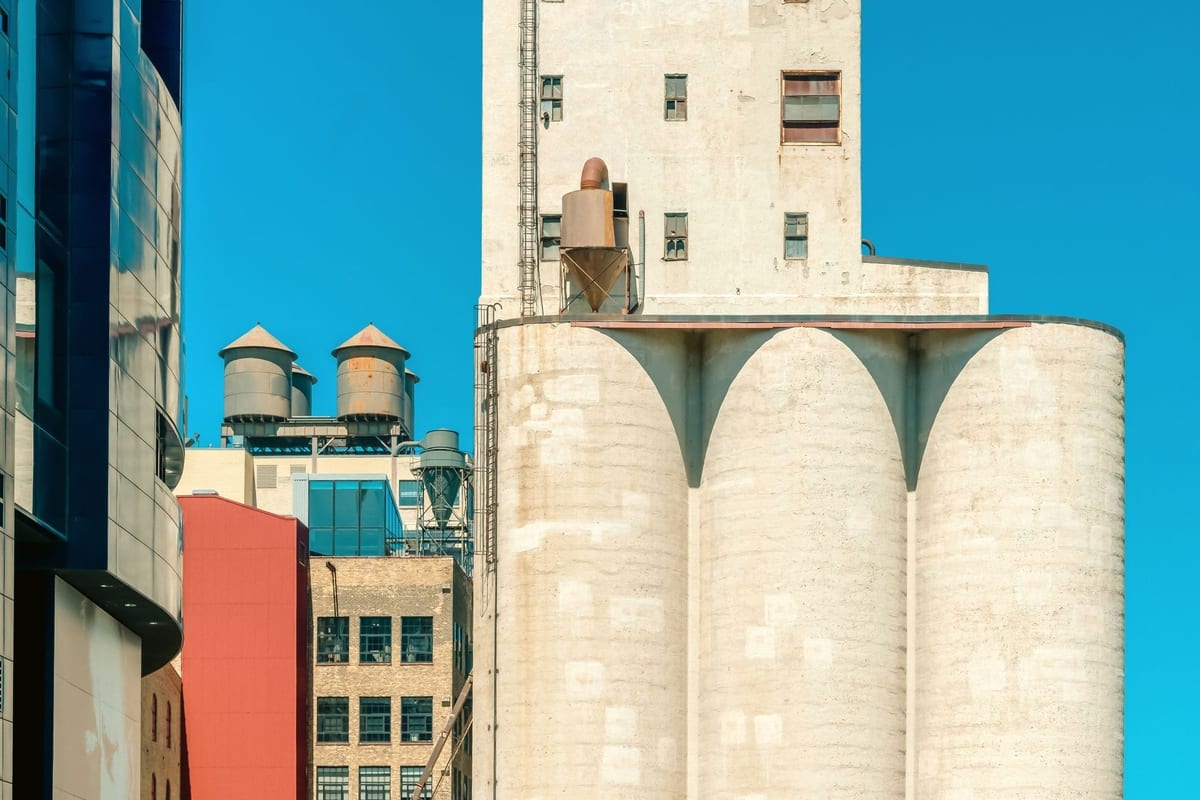 Tall white concrete grain silos beside brick and glass buildings under a bright blue sky
