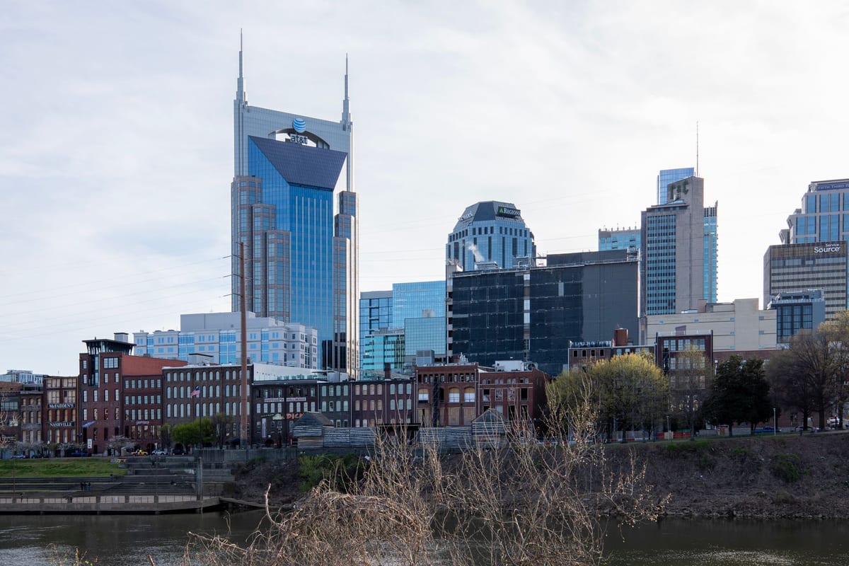 A skyline with a tower topped by two spires, behind a river and low brick buildings