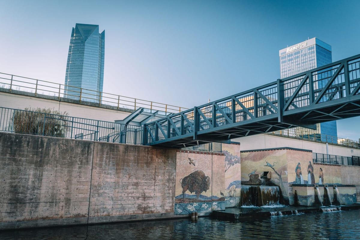 A glass tower and a steel footbridge over a concrete-walled canal