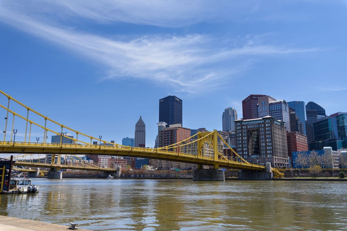 A yellow suspension bridge over a river, with downtown towers behind
