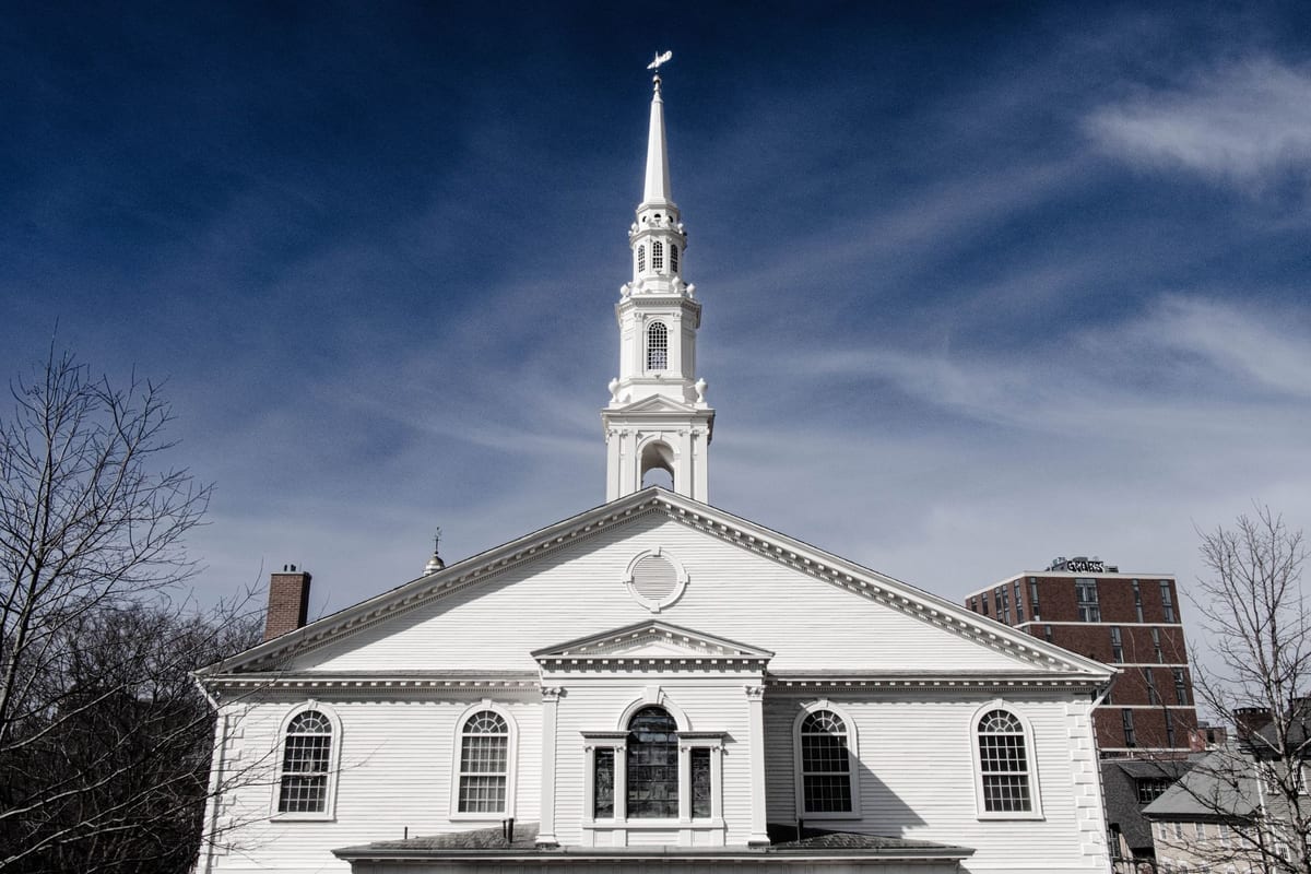 A white church steeple and columned portico under a blue sky with clouds