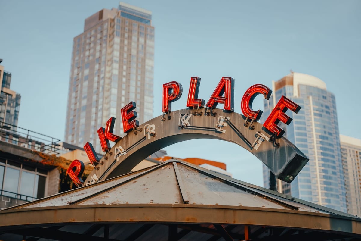 A large red neon sign arched over a market entrance, with high-rises behind