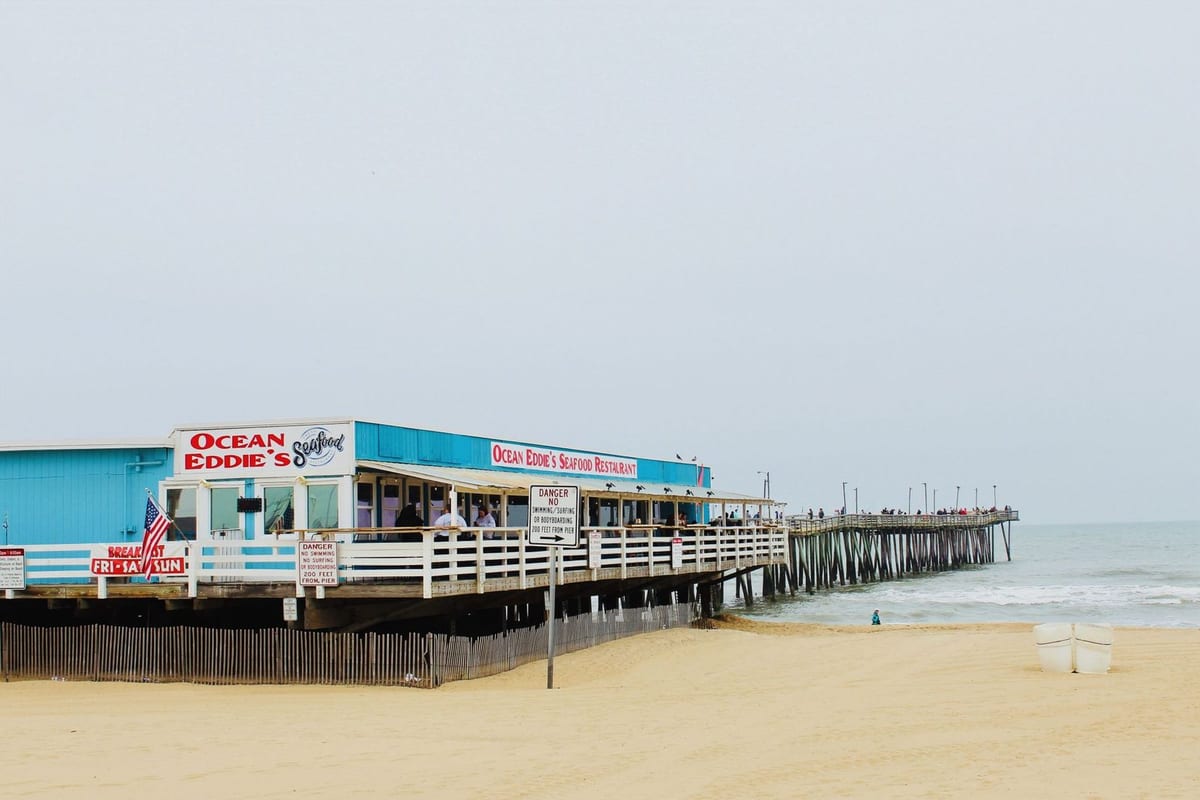 A fishing pier on a wide sandy beach, with a seafood restaurant at its foot