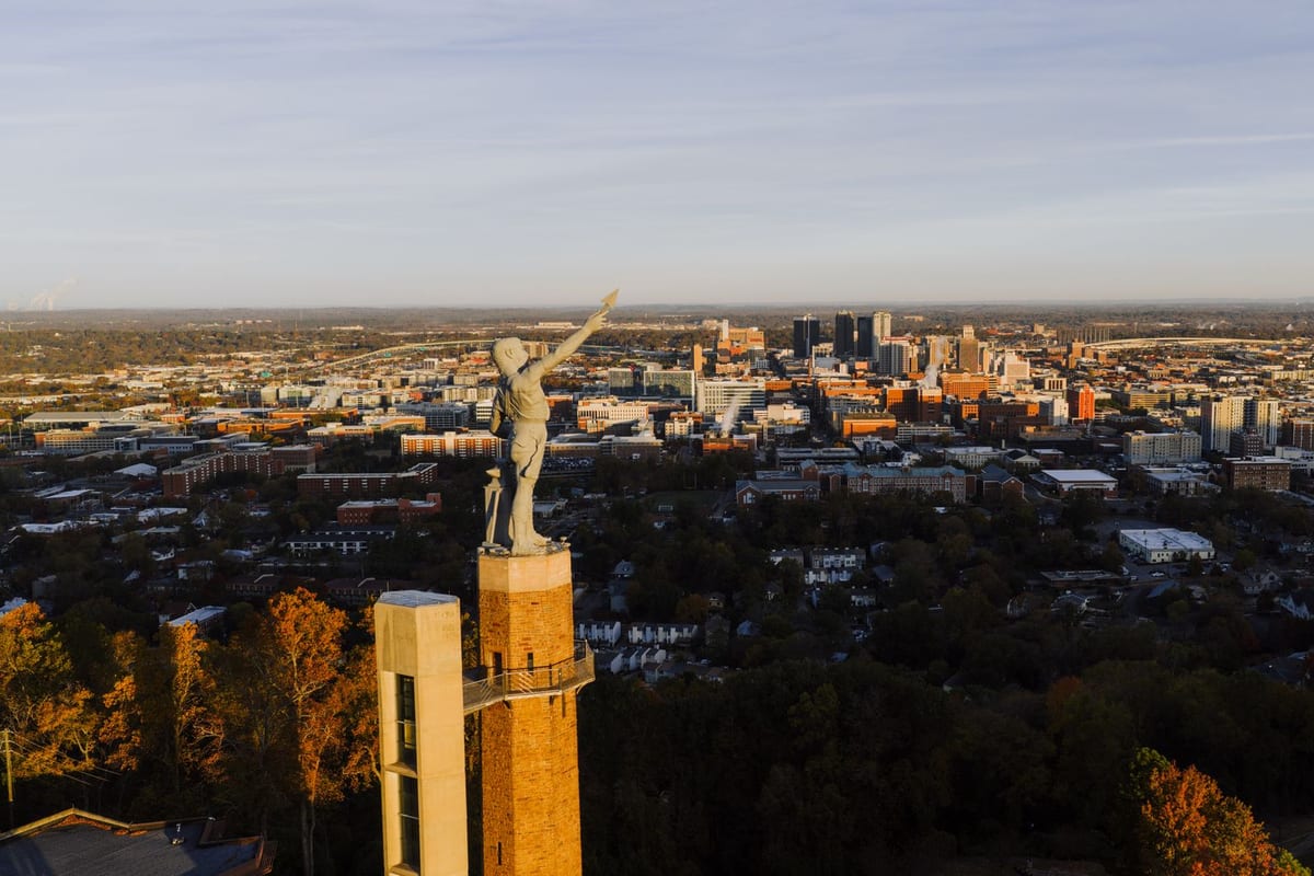 A statue on a tall column in the foreground, a flat city spreading to the horizon behind it