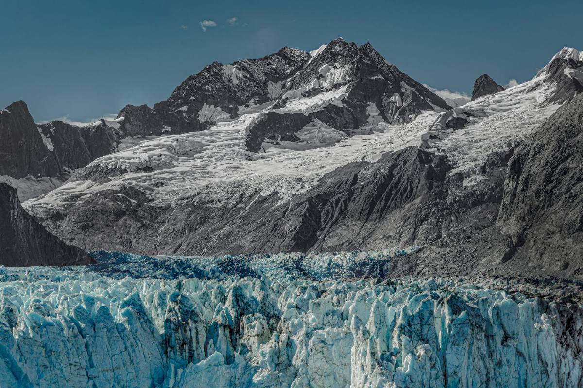 The broken blue-white face of a glacier below a ridge of rock and snow