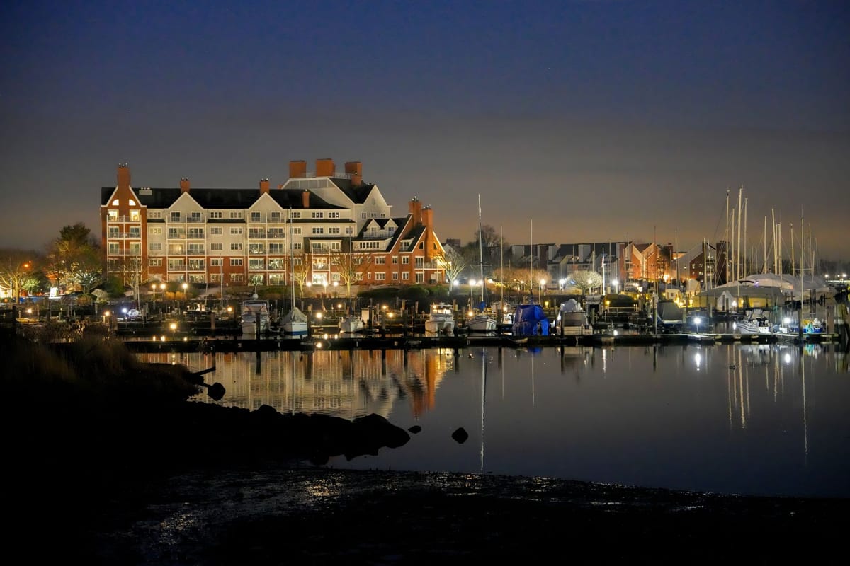 A lit hotel and a marina of sailboats reflected in still water at night