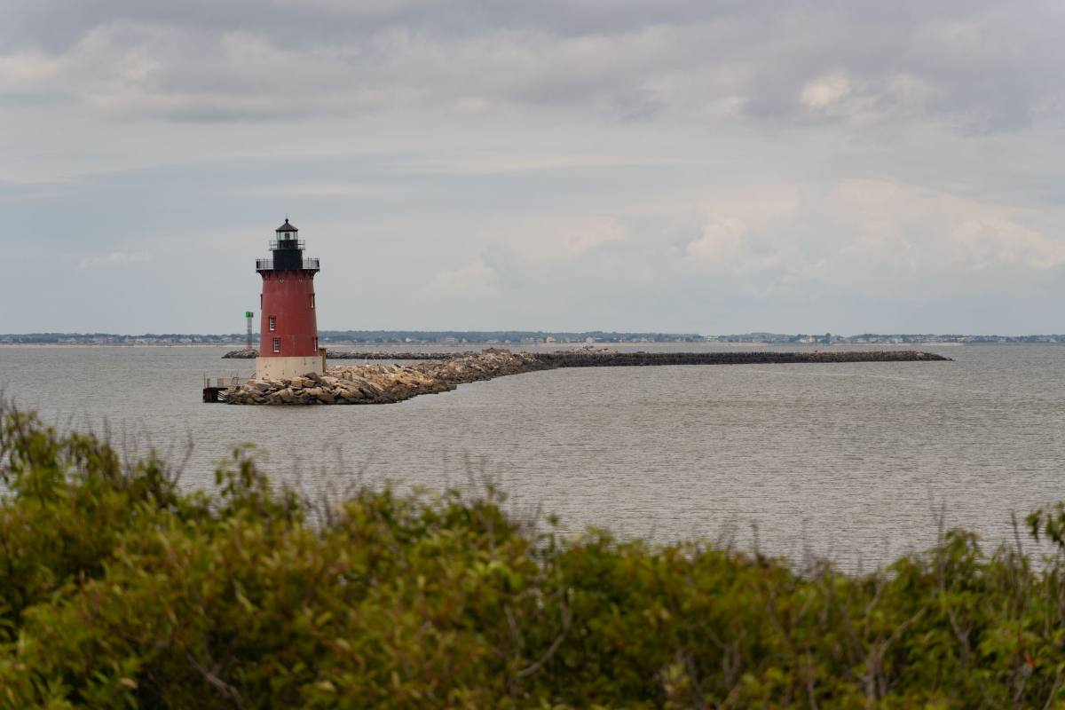 A small red lighthouse at the end of a stone jetty on gray open water
