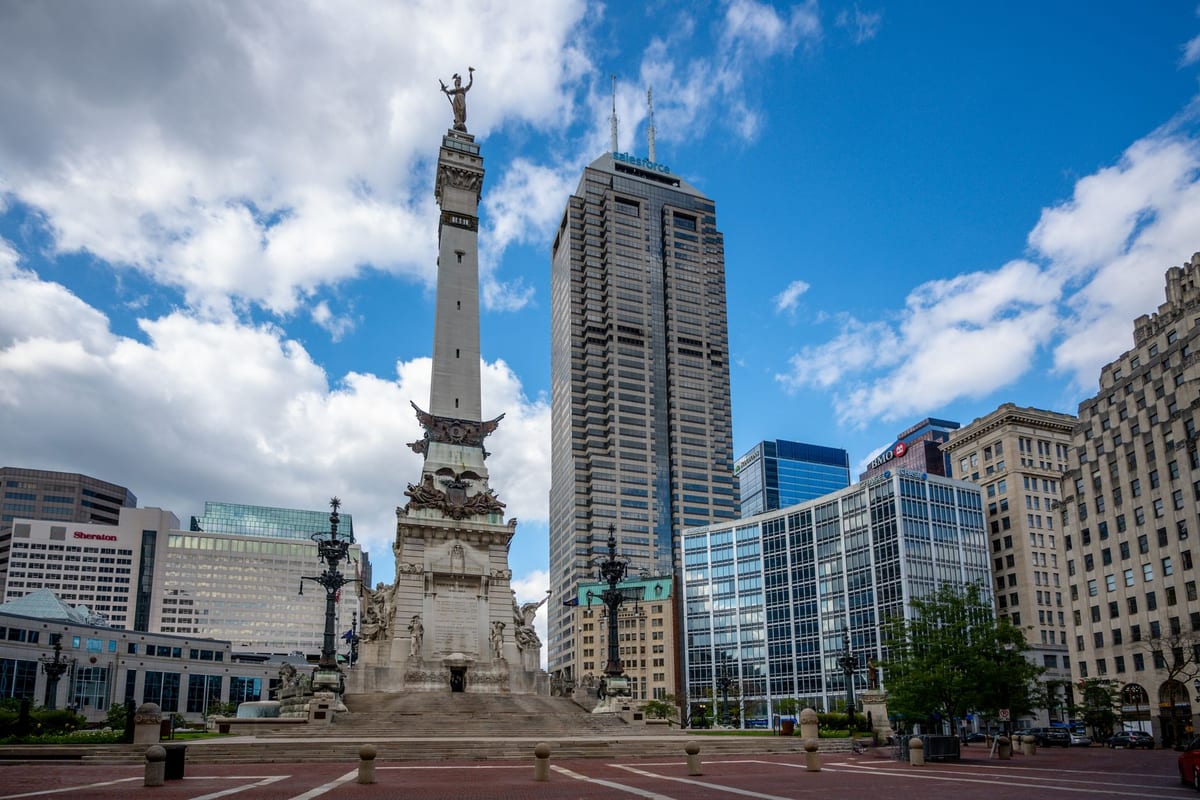 A tall stone monument in a round plaza, with office towers on either side