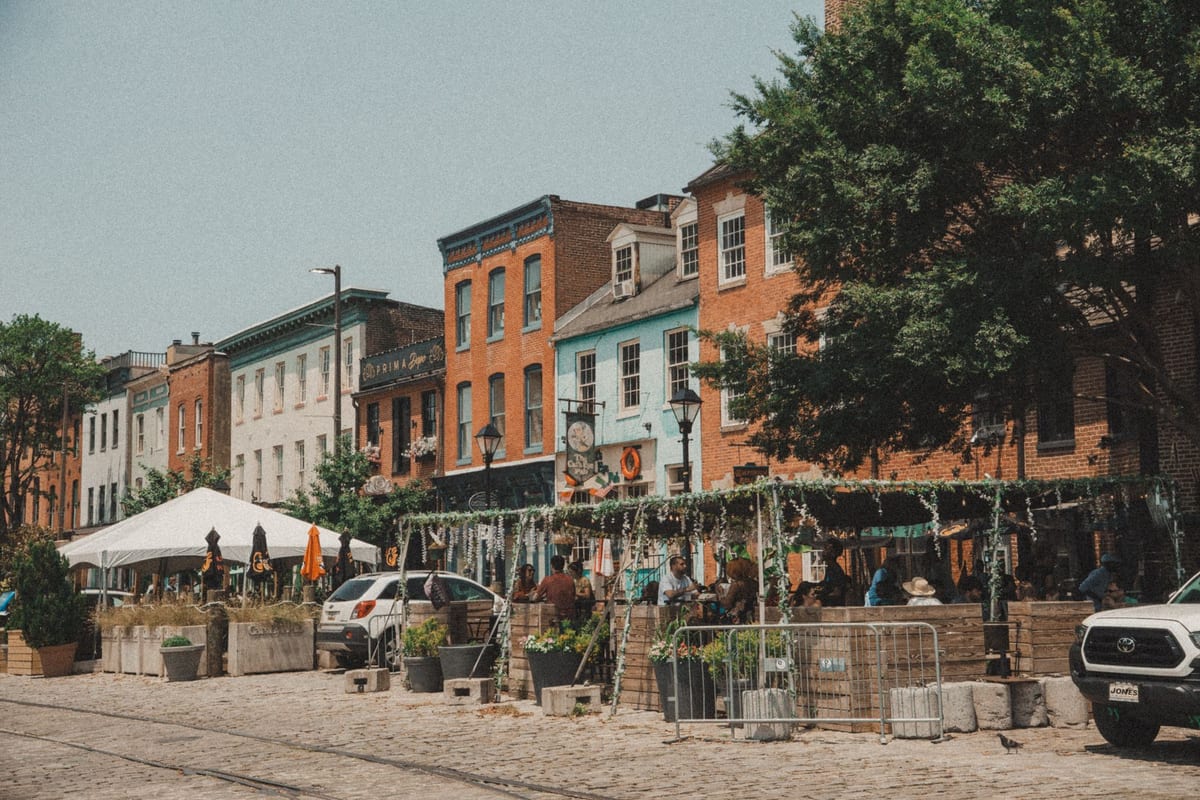 Brick row houses with outdoor tables and white umbrellas along a cobbled square