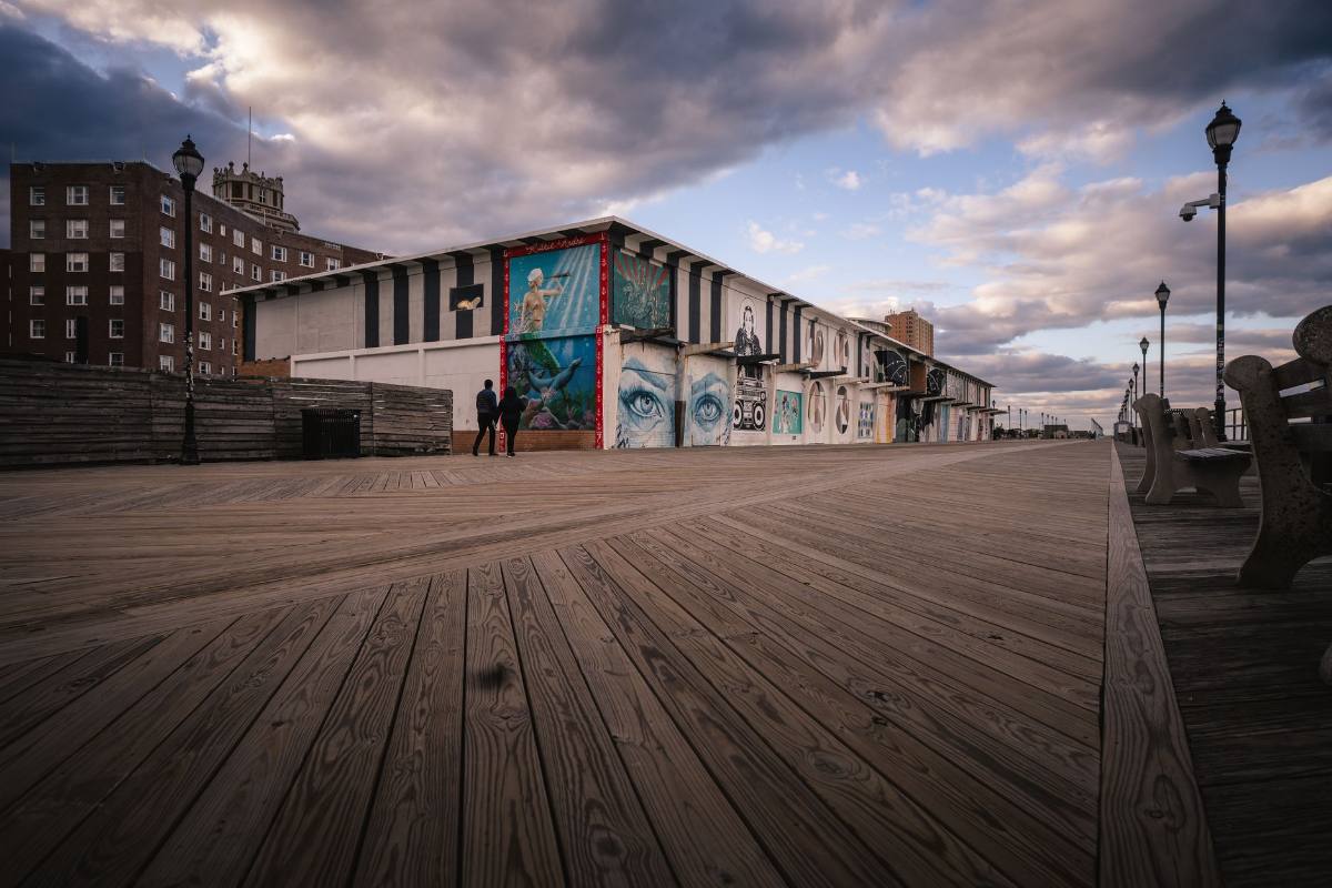 A wooden boardwalk under a dramatic sky, a mural-painted building at its end