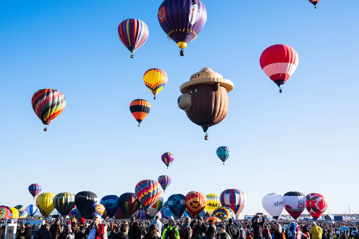 Dozens of hot air balloons rising into a clear sky above a crowd on a field