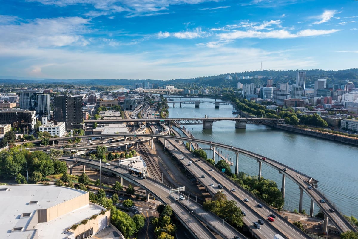A river city from above, railways and freeways running along the water toward the bridges
