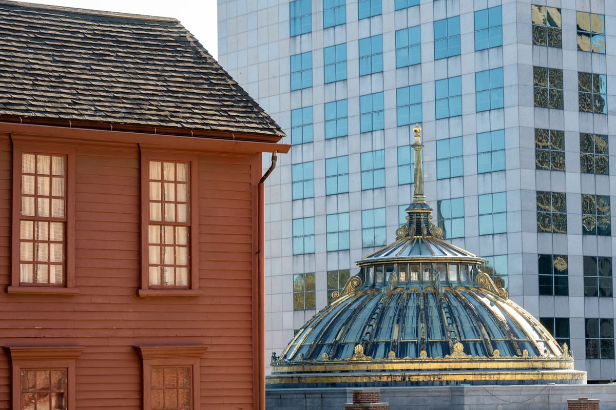 A red clapboard house beside a glass office tower and an ornate green dome