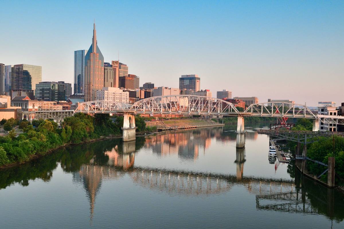 A skyline with a two-spired tower reflected in a river, a truss bridge in front