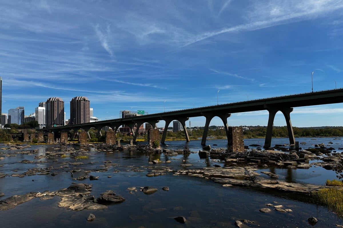 A long concrete railroad bridge crossing a rocky river toward a small skyline