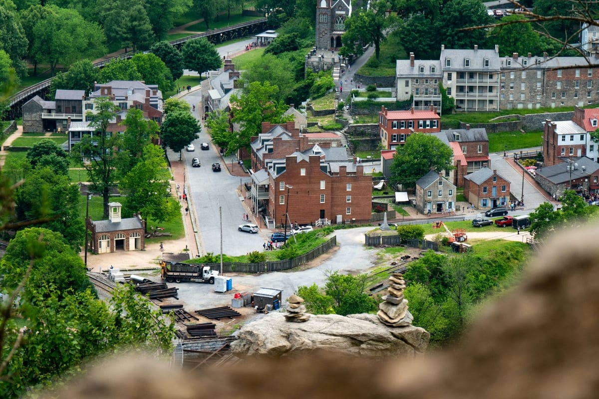 A small town of brick buildings and a steep street, seen from a wooded rock above